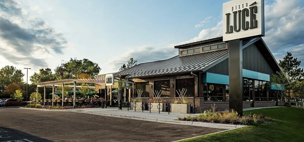 Modern Pizza Luce restaurant exterior with busy outdoor patio, soft evening light.