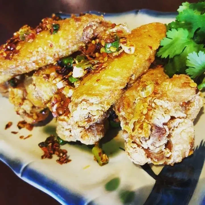 Fried chicken wings with garlic-chili sauce, garnished with green onions and cilantro.