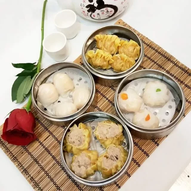 Four dim sum steamers with assorted dumplings on a bamboo mat.