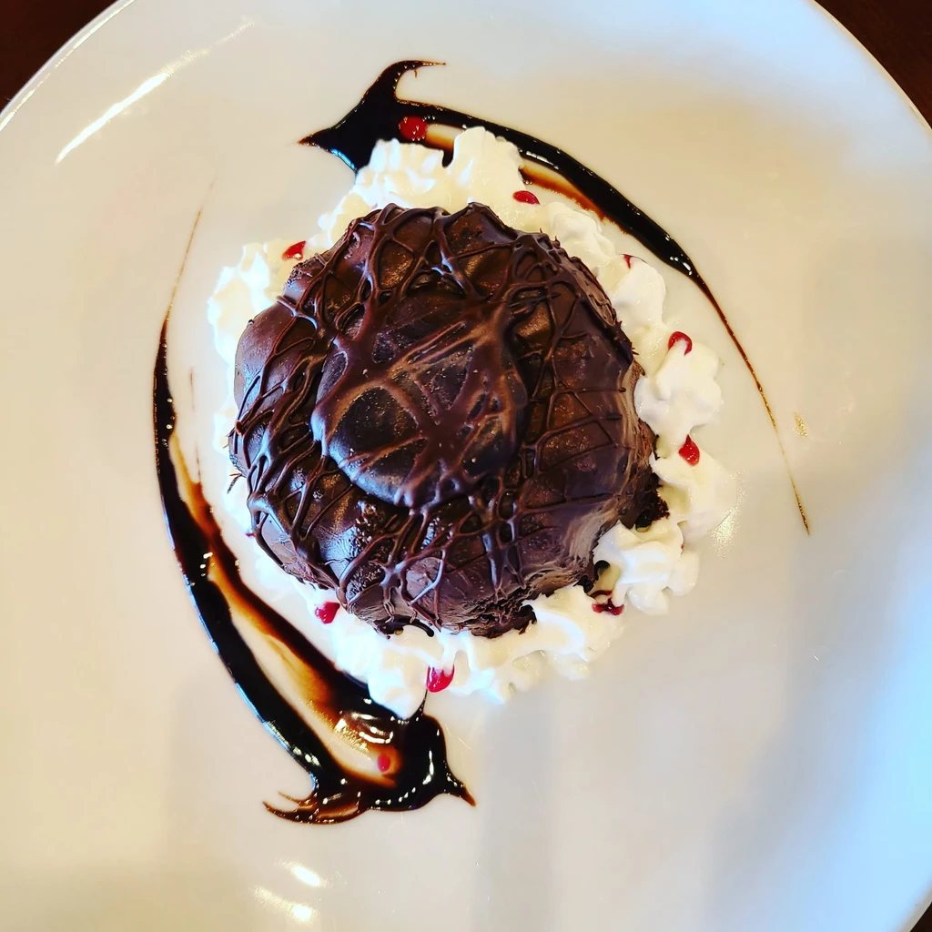 Spherical chocolate dessert with glaze, whipped cream, and berry garnish.