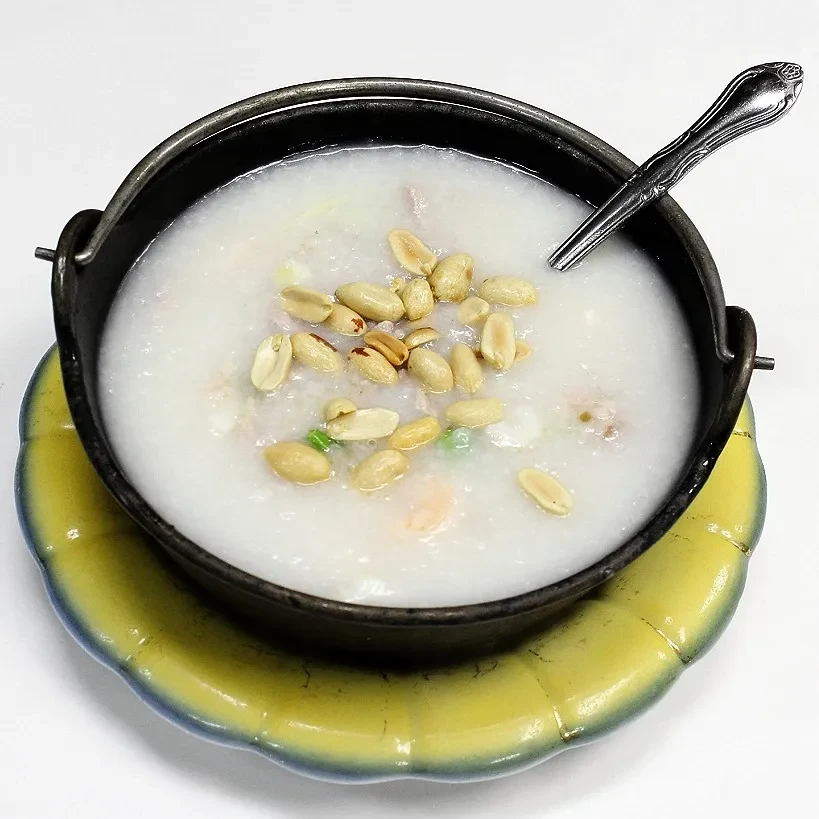 Congee with peanuts, meat, green onions in a dark bowl on yellow plate.
