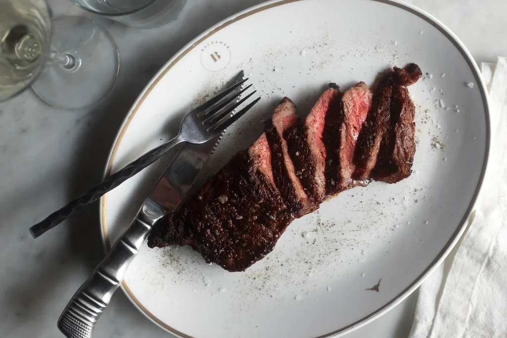 Top-down: Sliced medium-rare steak, salt, pepper on a white plate.