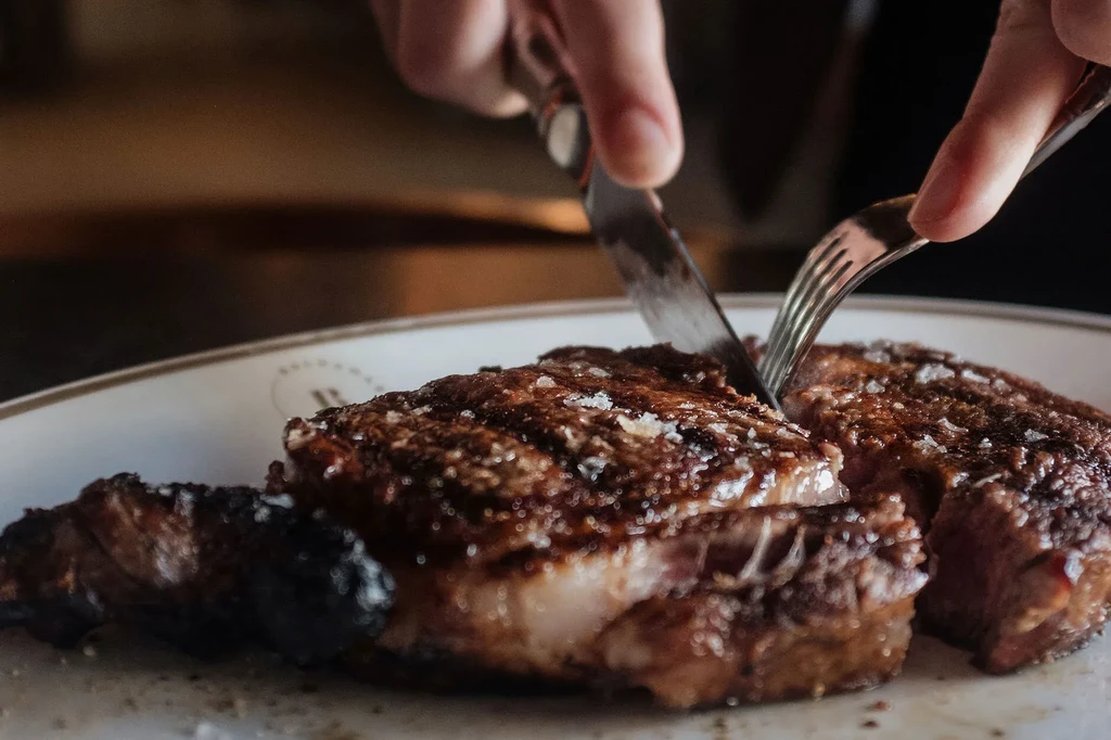 Close-up of hands cutting seared medium-rare steak on a white plate.