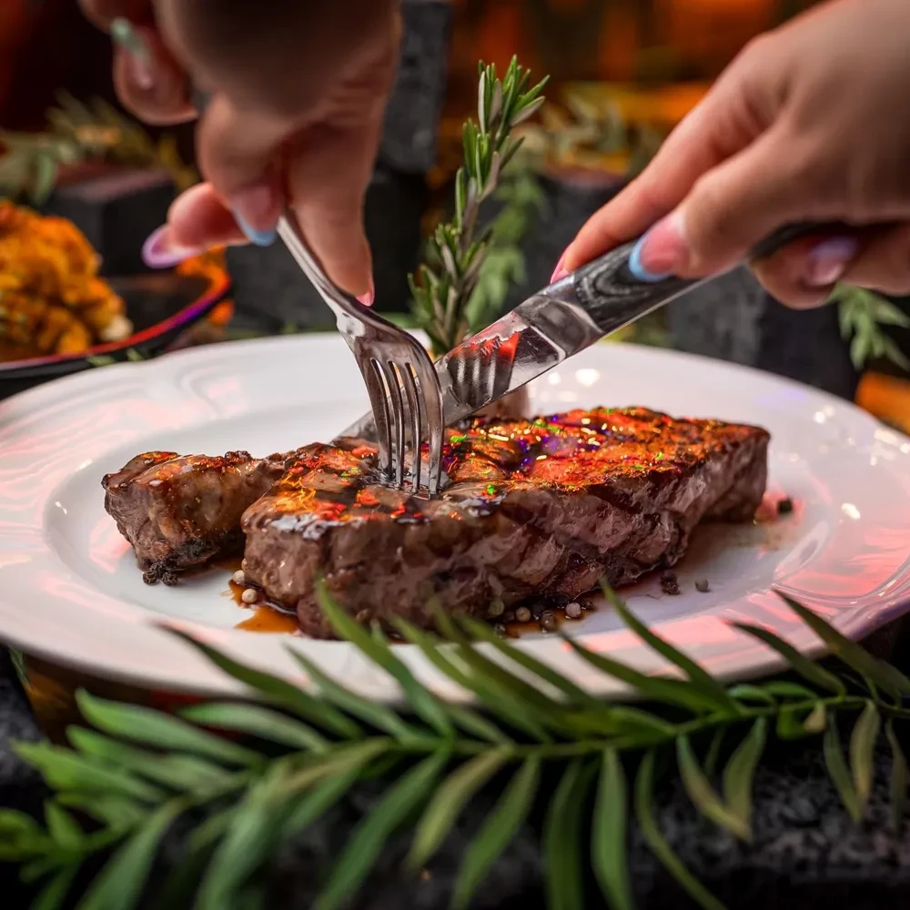 Hands cutting a grilled steak with glistening glaze and rosemary.