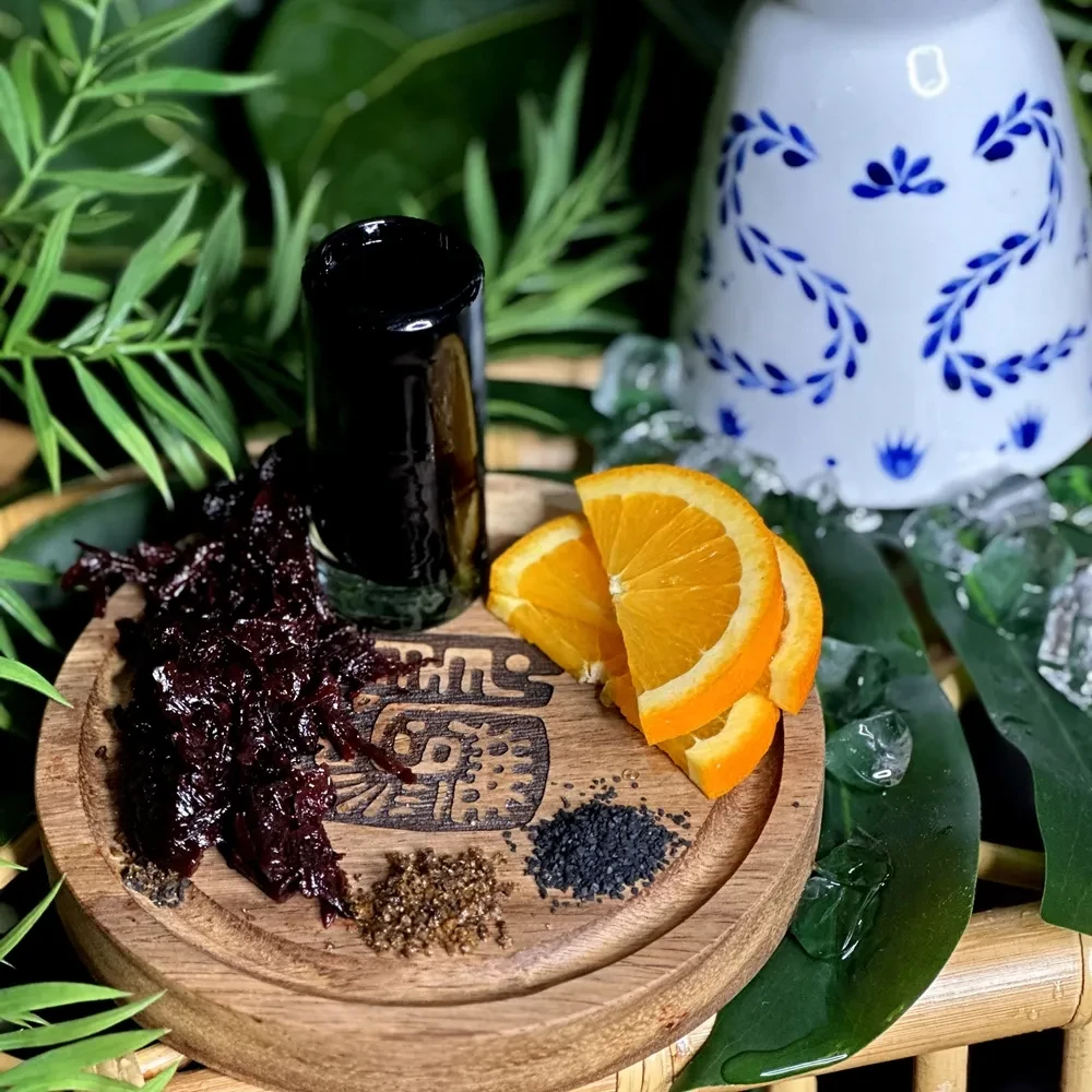 Dark liquid shot, hibiscus, salts, orange slices, on wooden board.
