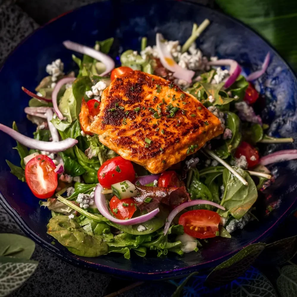 Seared salmon over salad with tomatoes, onion, cucumber, and cheese.
