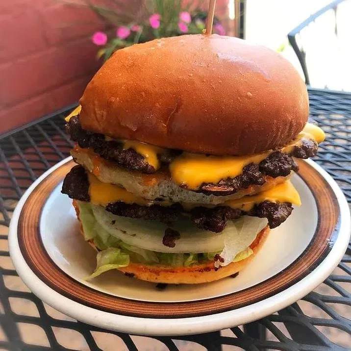 Large stacked burger with multiple patties, melted cheese, lettuce, and onion.