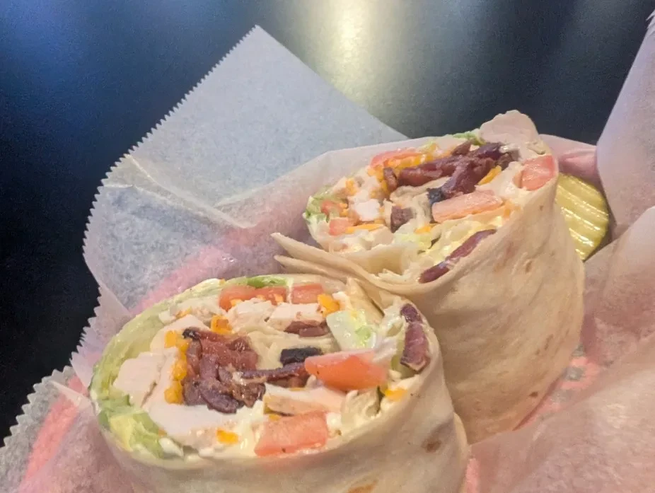 Close-up of halved chicken bacon wrap in a basket with a pickle.