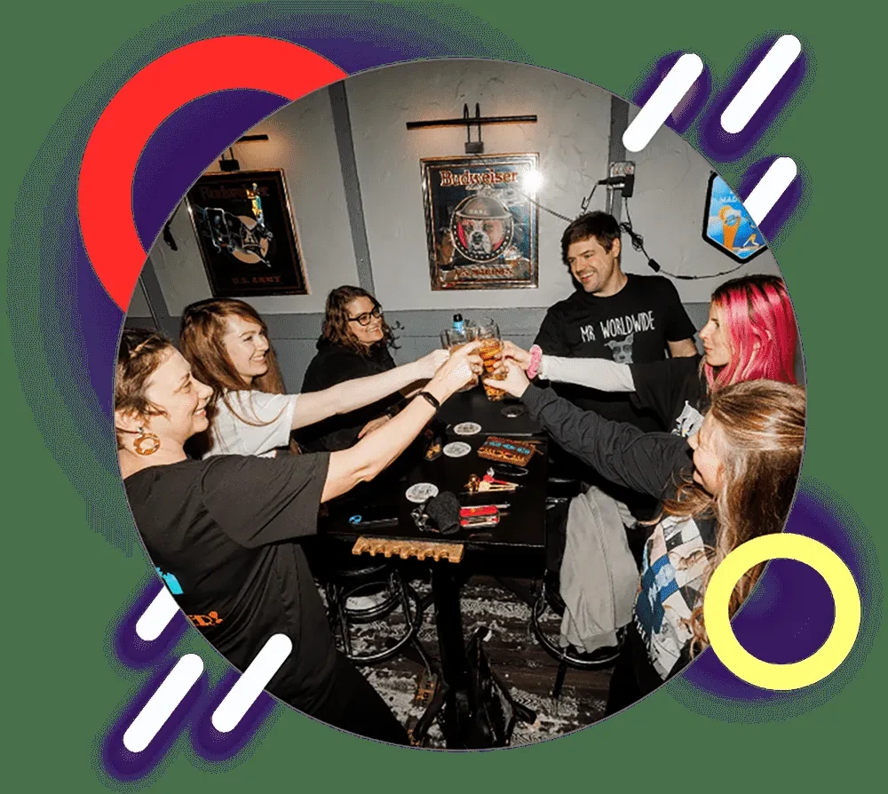 Six smiling people toast with beer glasses in a lively bar.