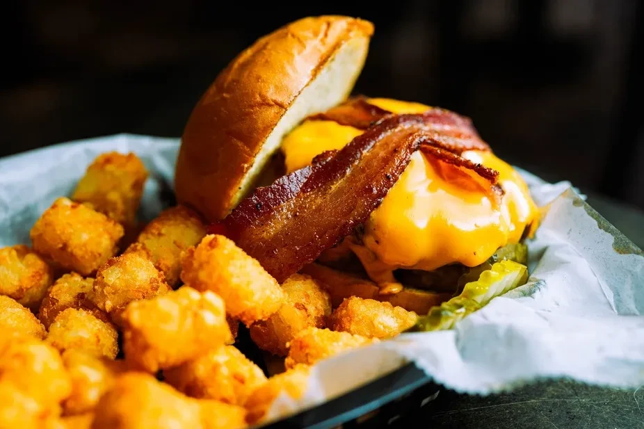 Gourmet burger with melted cheese, bacon, pickles, and crispy tater tots.