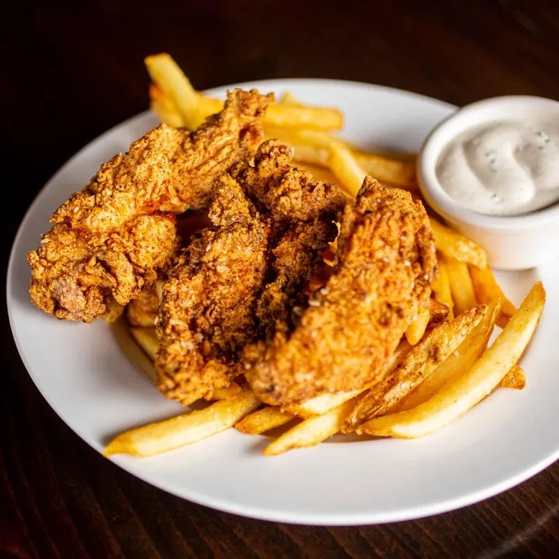 White plate with golden fried chicken tenders, fries, and dipping sauce.