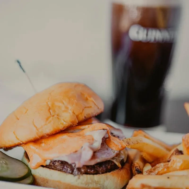 Gourmet burger with bacon, melted cheese, fries, pickles, and Guinness.