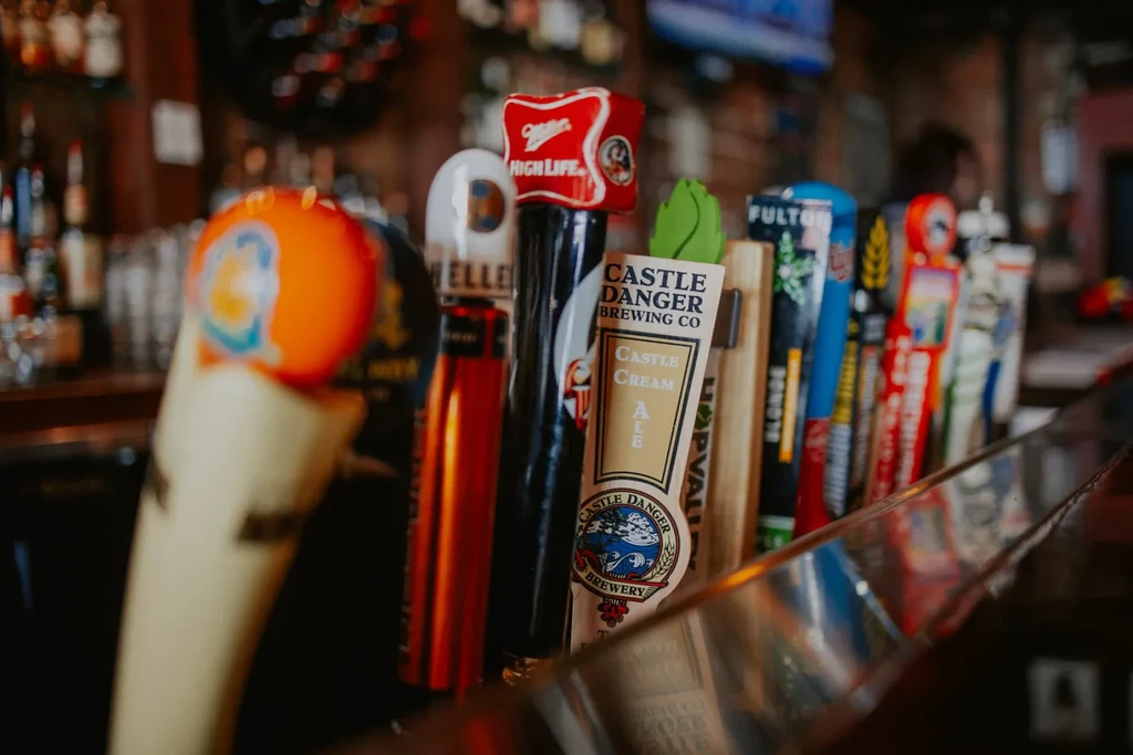 Close-up of beer taps: Castle Cream Ale, Miller High Life, and others blurring.