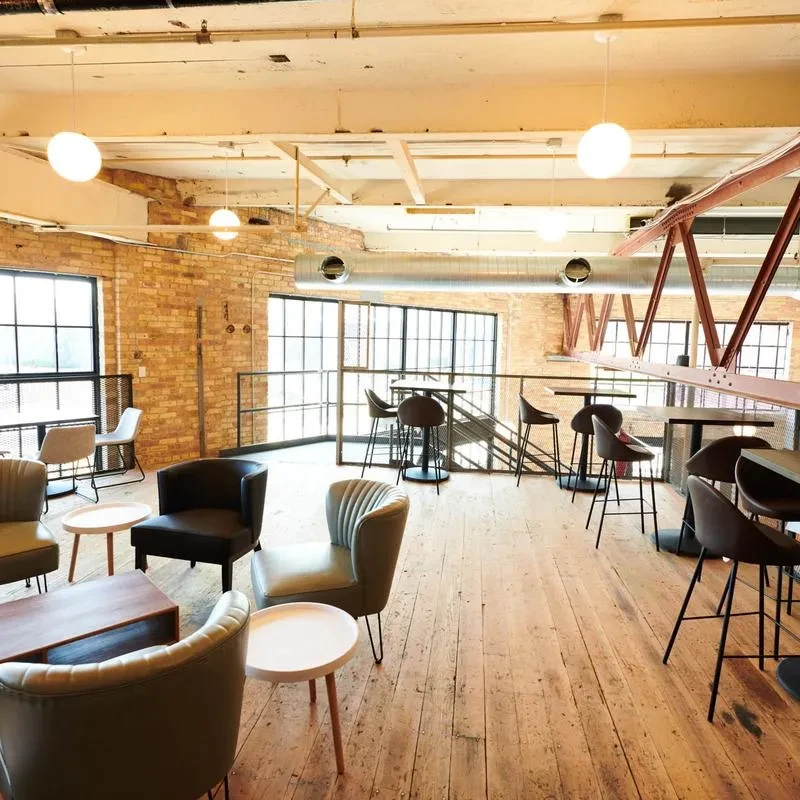 Modern-industrial restaurant interior with exposed brick, large windows, and varied seating.