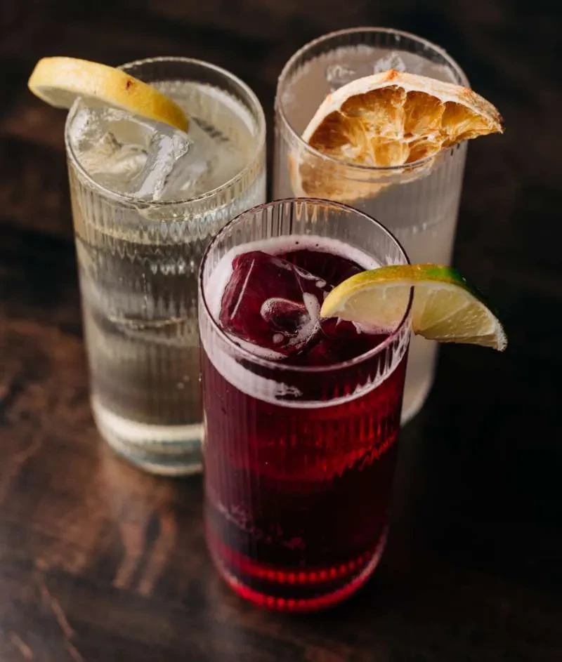 Three textured glasses with colorful iced drinks and fruit garnishes.