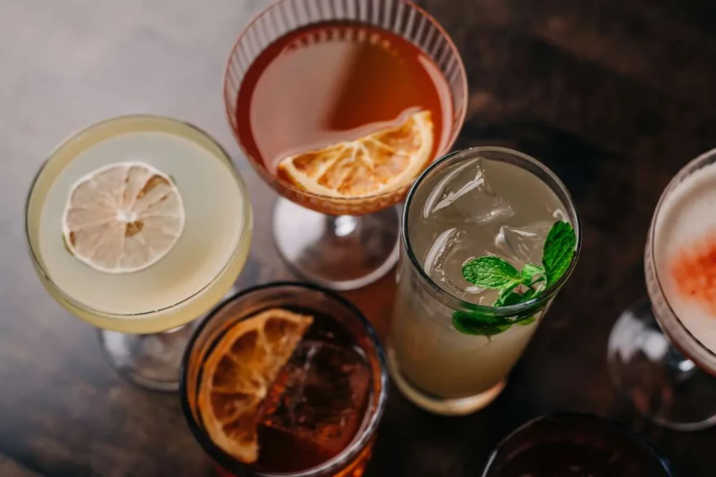 Overhead view of five varied cocktails with garnishes on a dark table.