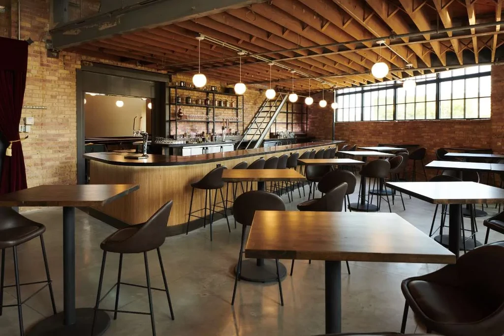 Modern bar interior with exposed brick, wooden beams, concrete floor, curved bar.