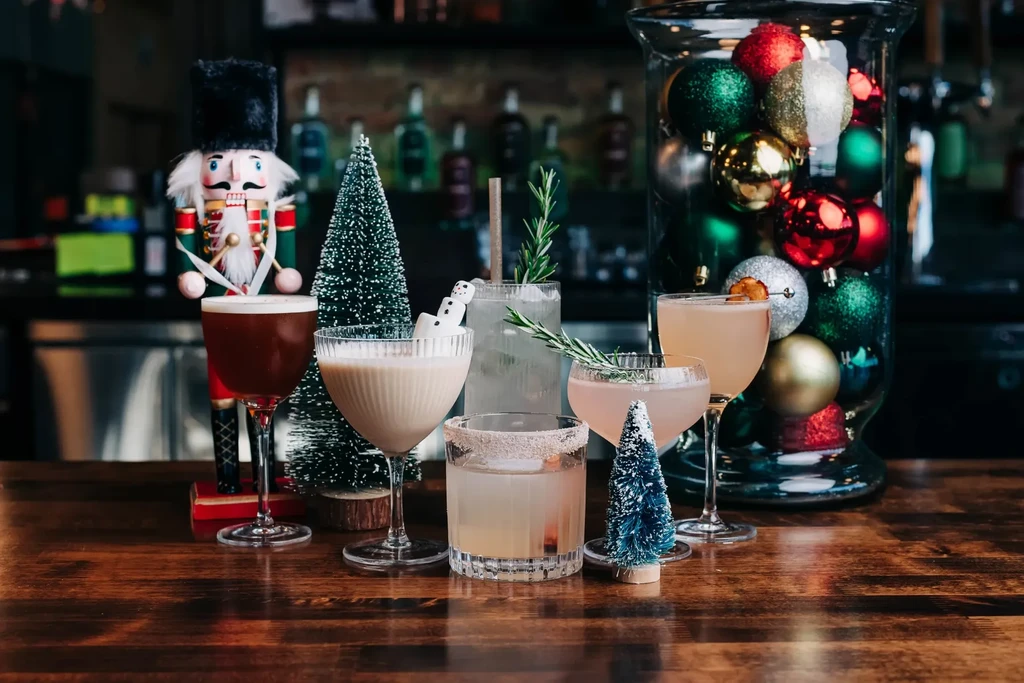 Five festive cocktails with Christmas decorations on a wooden bar.