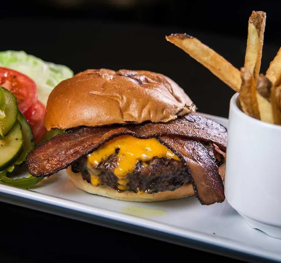 Close-up cheeseburger with melted cheese, bacon, pickles, and golden fries.