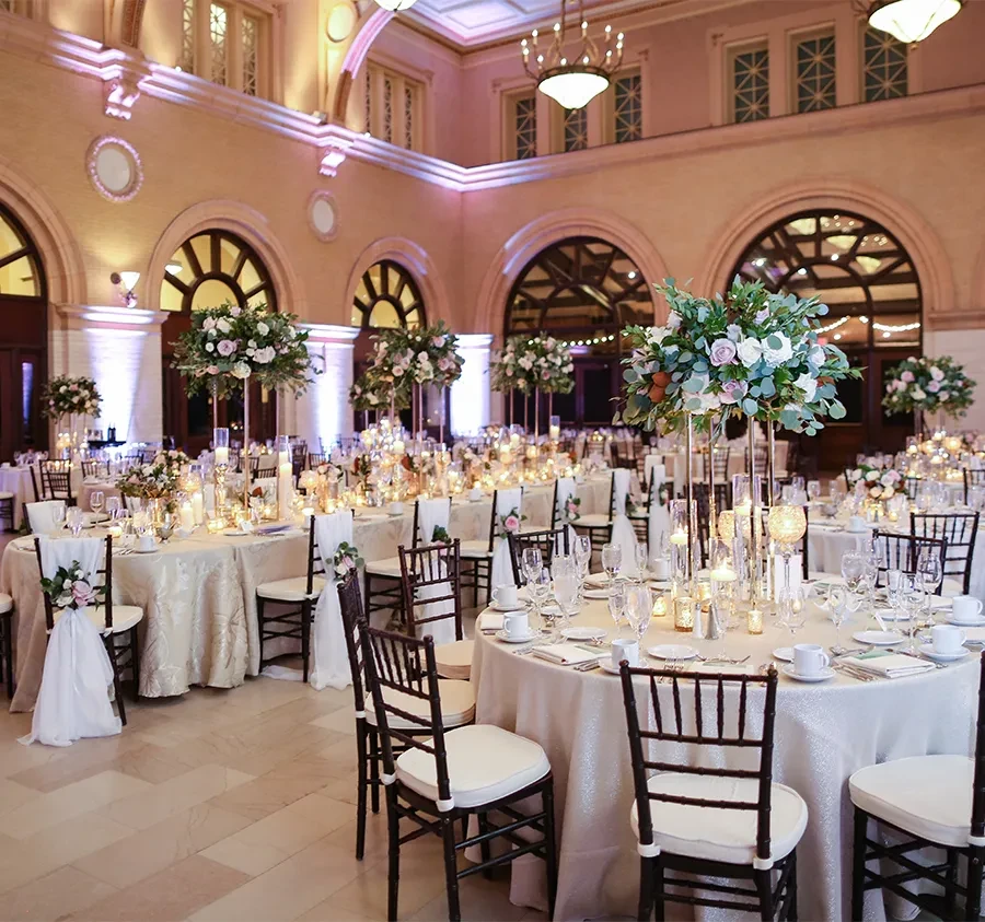 Decorated ballroom with floral tables, candles, and purple uplighting for an event.