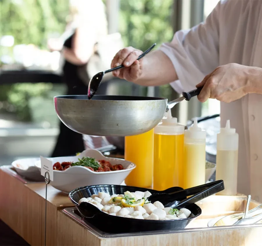 Chef's hands stir food in a pan at a well-stocked buffet station.