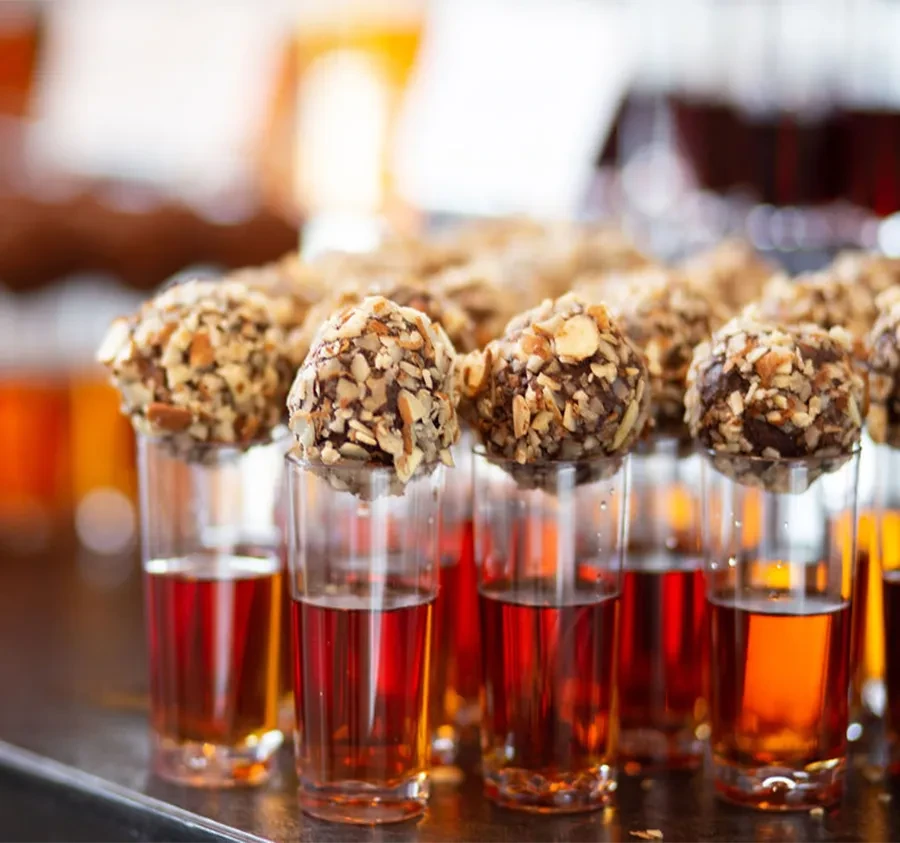 Rows of shot glasses with reddish liquid, topped with nut truffles.