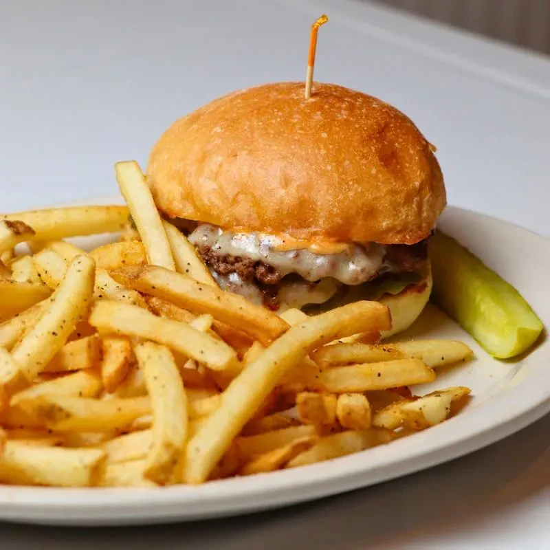 Cheeseburger, golden seasoned fries, and a pickle on a white plate.