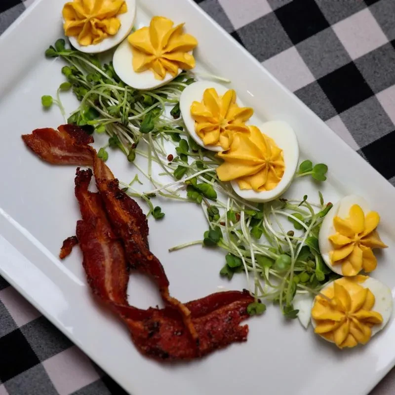 Piped deviled eggs, crispy bacon, microgreens on a white plate.