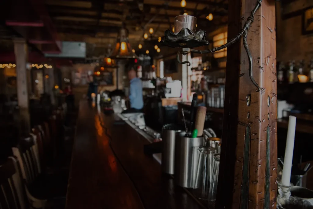 Dark carved wooden pillar, lit candle, and blurred rustic bar.