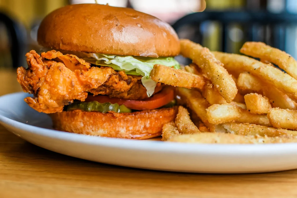 Fried chicken sandwich with lettuce, tomato, pickles, and crispy fries.