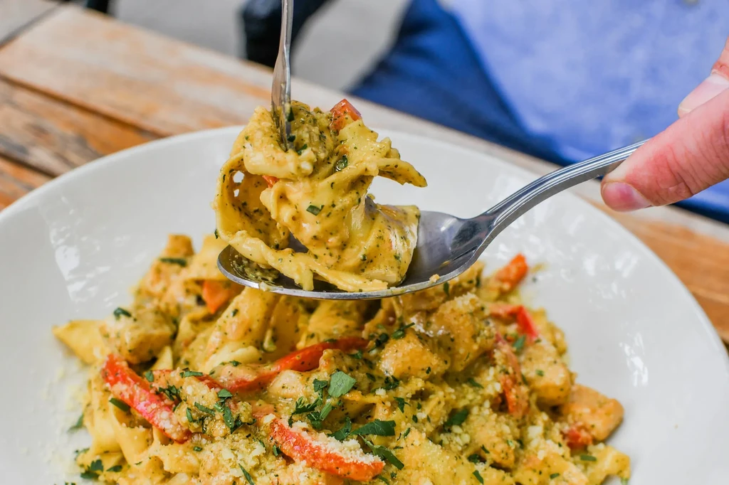 Hand lifts creamy pesto pasta with chicken and bell peppers.