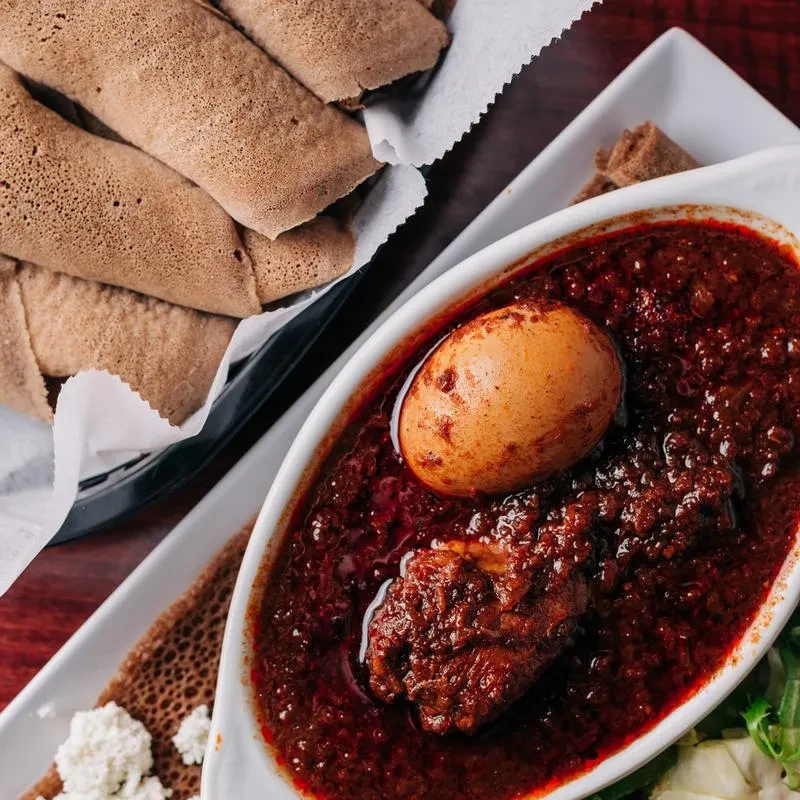 Overhead view: Ethiopian Doro Wat, egg, injera, and crumbled cheese.