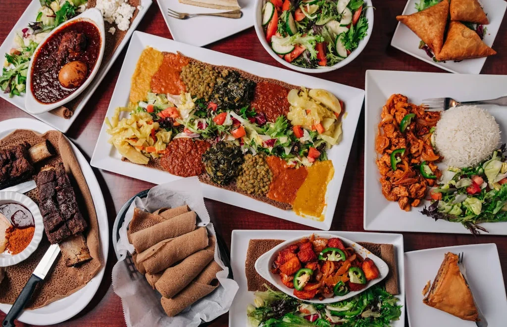 Large spread of colorful Ethiopian/Eritrean dishes with injera, stews, and sides.