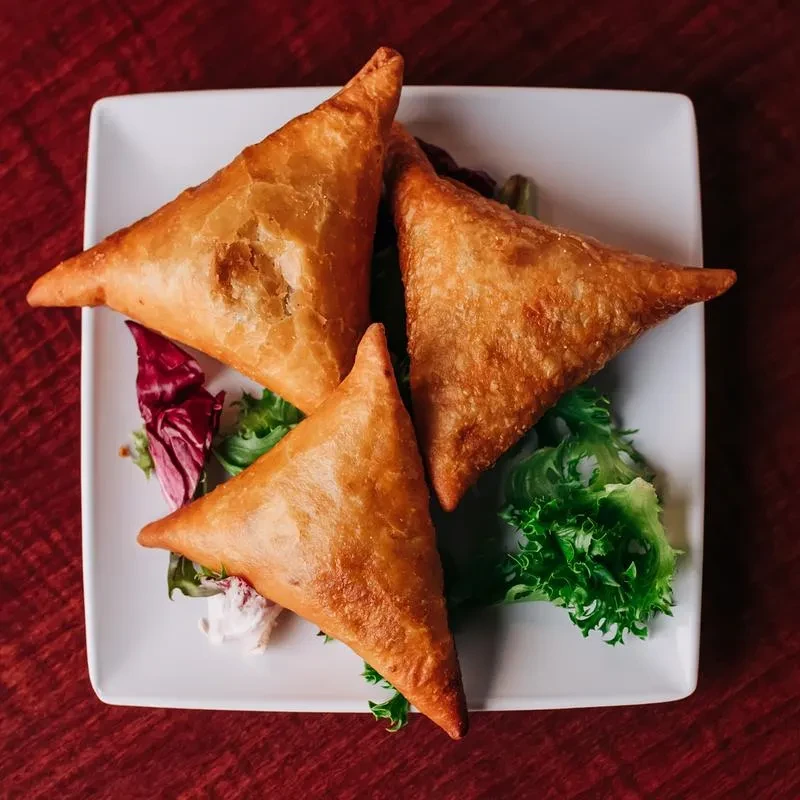 Three golden-brown fried triangular pastries with greens and creamy dip.