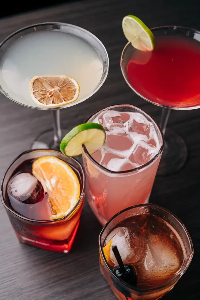 Five vibrant, garnished cocktails in various glasses on a dark background.