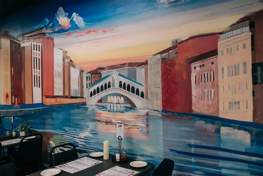 Restaurant interior with Venetian canal mural and set dining tables.