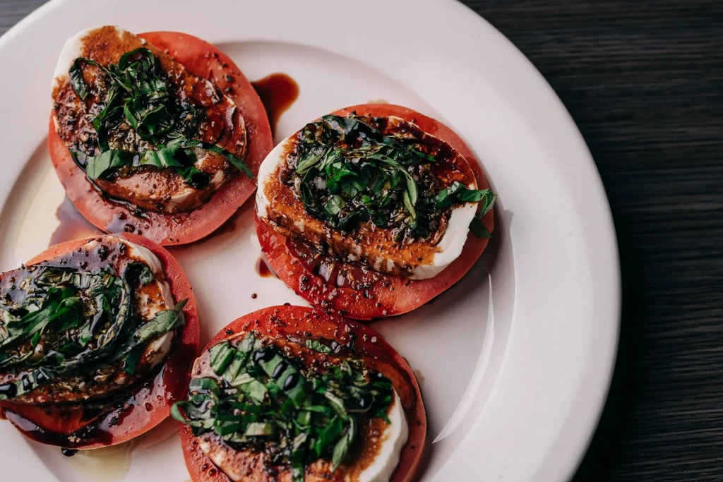 Four Caprese salad portions with tomato, mozzarella, basil, balsamic glaze.