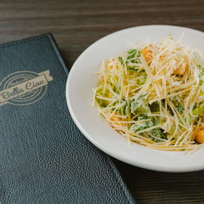 Close-up of Caesar salad on a plate next to a Bella Ciao menu.