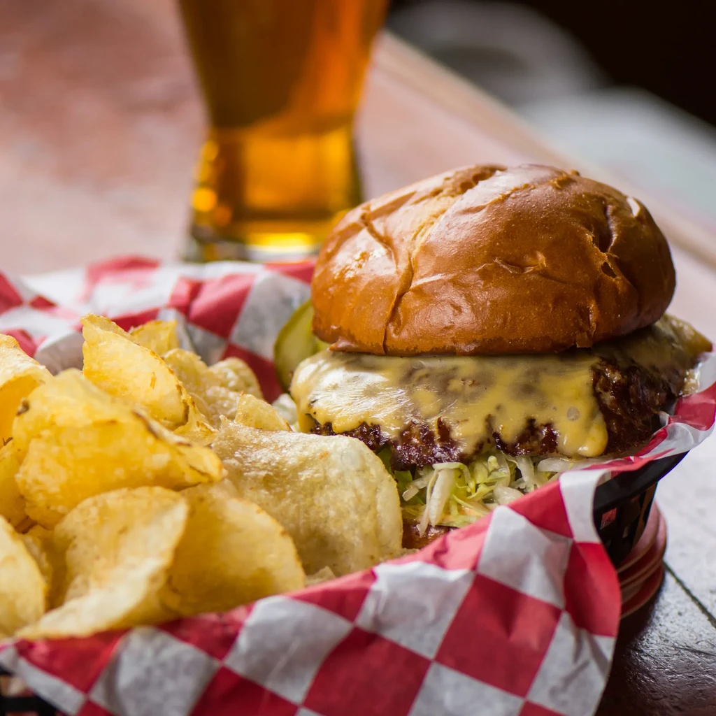 Cheeseburger and golden potato chips in a red checkered basket.