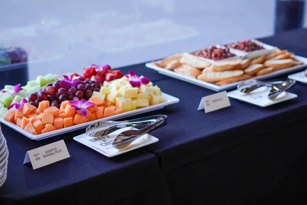 Buffet table with fruit, cheese, bruschetta platters, and serving tongs.