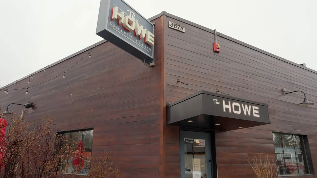 Modern restaurant The Howe exterior, dark wood, illuminated sign, string lights.