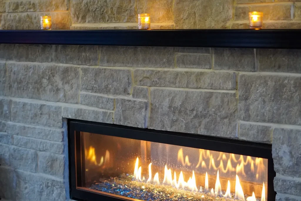 Modern stone fireplace with orange flames, glass pebbles, and lit votives.