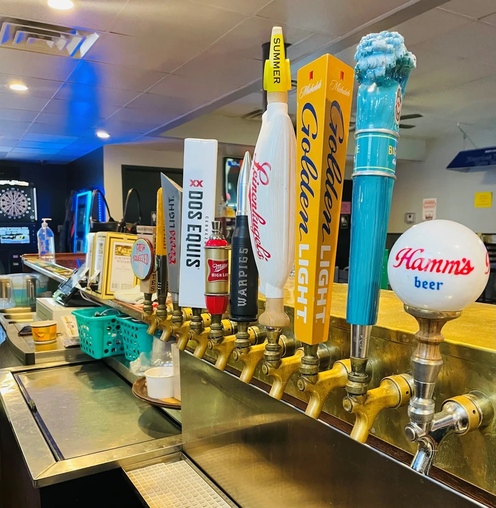 Close-up of nine distinct beer tap handles on a brass bar manifold.