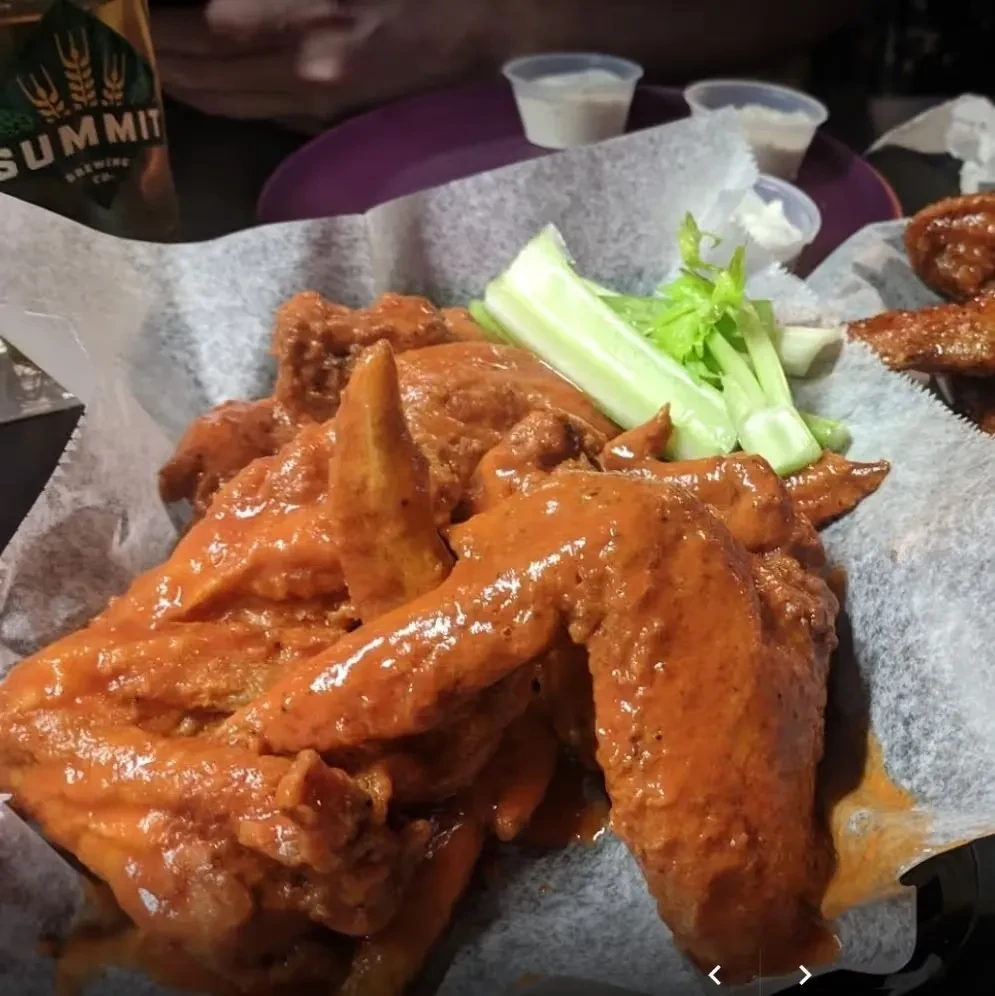 Close-up of buffalo chicken wings, celery, dipping sauces, and a beer.