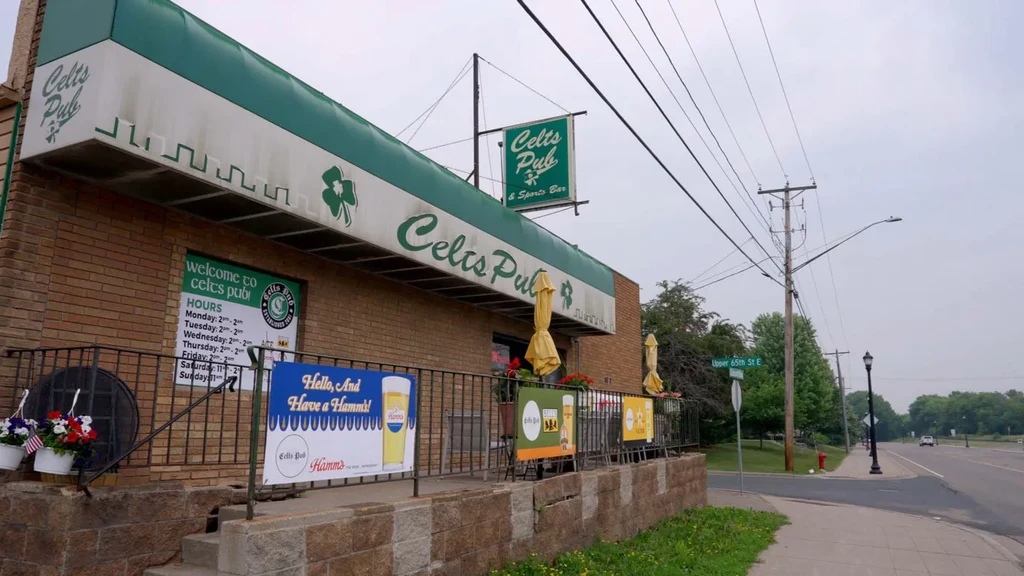 Celts Pub: brick building, green awning, patio with yellow umbrellas.