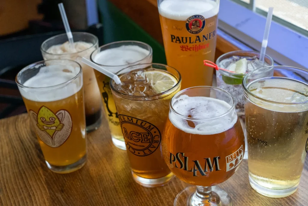 Eight assorted beers and cocktails with logos displayed on a wooden table.