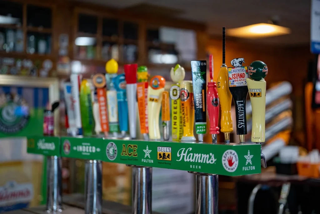 Row of colorful beer tap handles featuring various brand names at a bar.