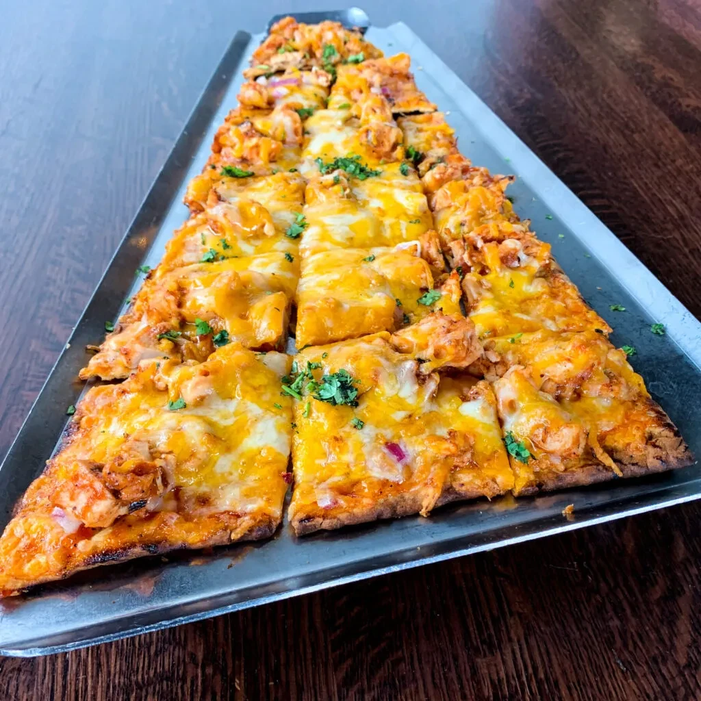 Rectangular flatbread pizza with buffalo chicken, cheese, onion, and herbs.