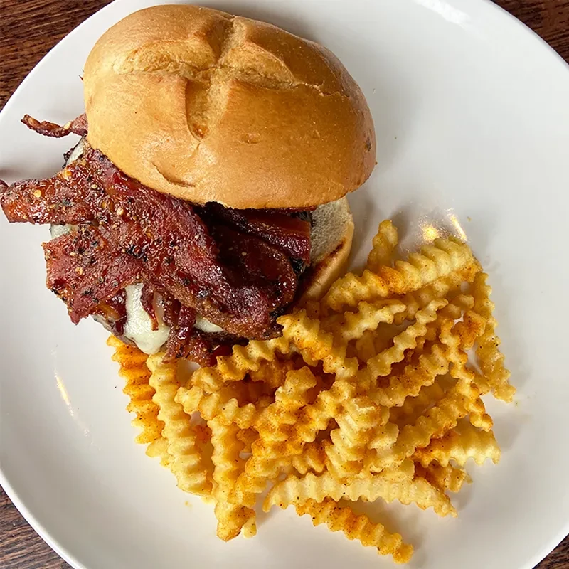 Kaiser burger with melted cheese, bacon, and seasoned crinkle-cut fries.