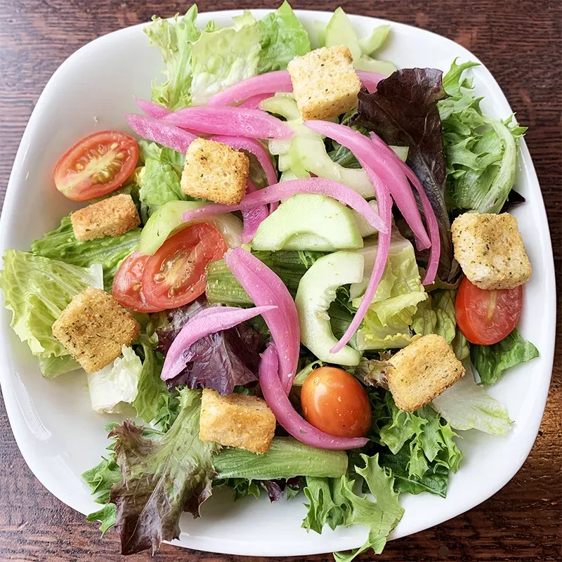 Top-down salad with mixed greens, tomatoes, cucumber, pickled onions, croutons.